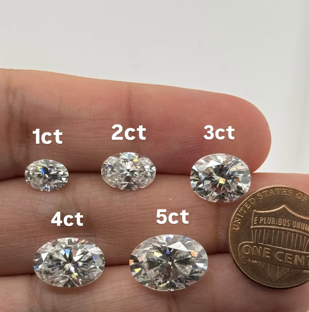 Oval diamonds of 1, 2, 3, 4 and 5 carats held on a fingertip next to a US penny for scale